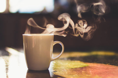 Close up of steaming cup of coffee or tea on vintage table - early morning breakfast on rustic background