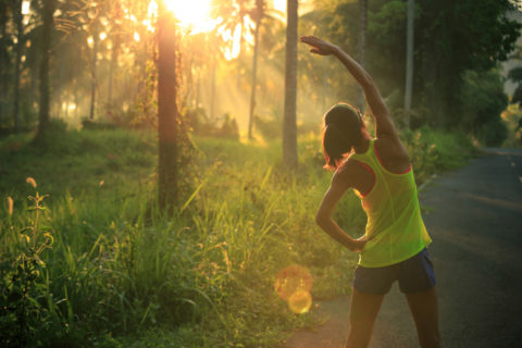 Young female runner warming up before running at morning forest trail