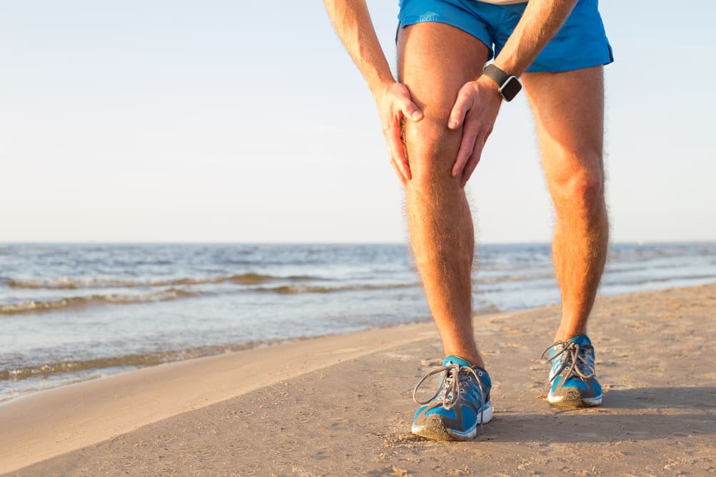 Man running on beach expressing knee pain