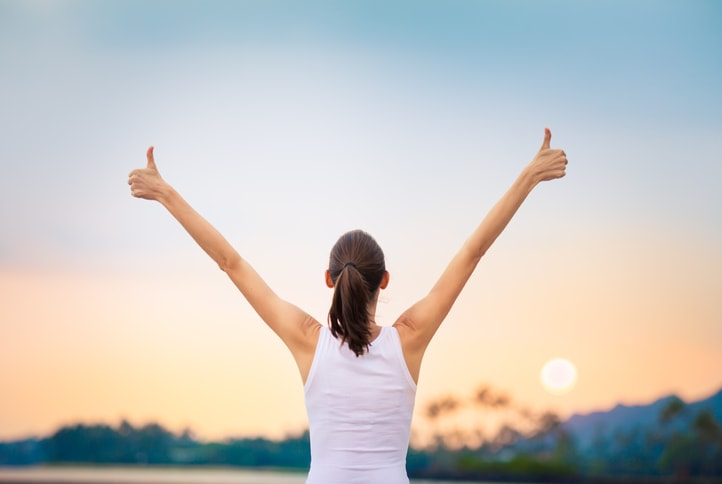 Woman giving thumbs up while viewing sunset