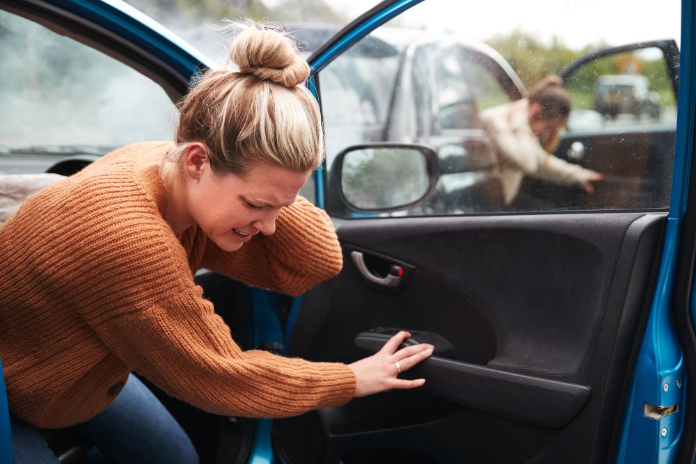 Woman exiting car from passengers side with neck pain after being in a car accident