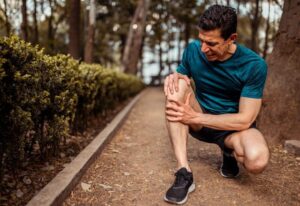 Older man expressing knee pain while on a walk outside in Maryland